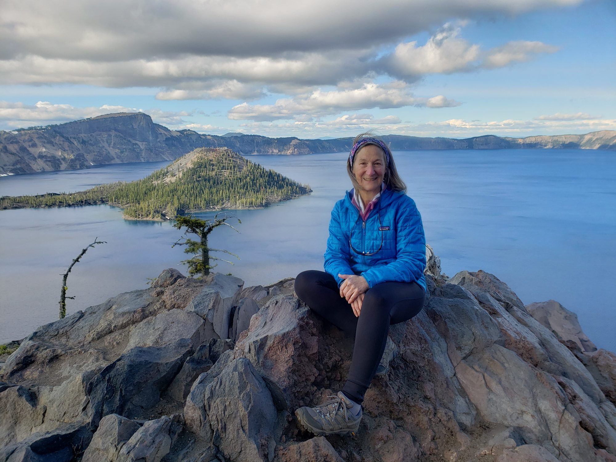 Debra Mailman sits atop a stone outcropping in front of a body of water. 